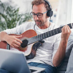 Mann lernt Gitarre auf dem Sofa