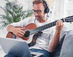 Mann lernt Gitarre auf dem Sofa